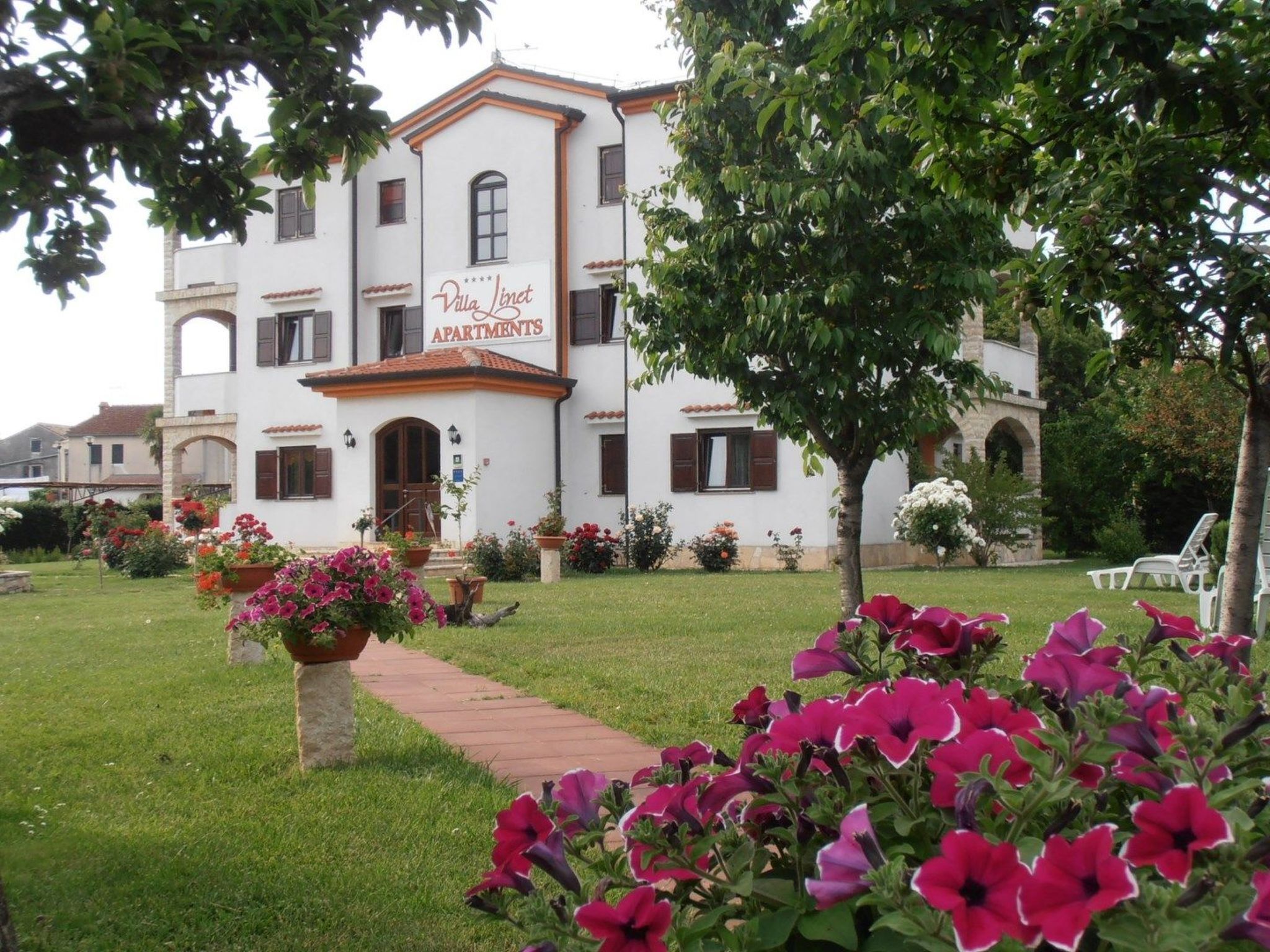 Apartamentos Villa Linet con entrada al jardín, un camino y macizos de flores.
