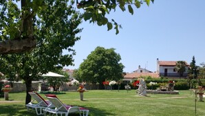 Un jardín bien cuidado con una estatua, una fuente y un edificio con techo de tejas al fondo.