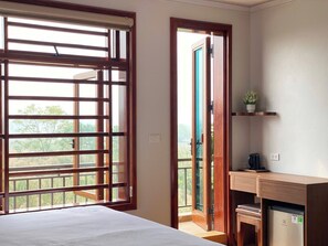 Une chambre comprenant un lit, un bureau avec un ordinateur, un petit réfrigérateur et une fenêtre avec des stores.