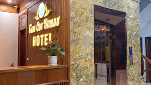 Een hotel receptie met een houten balie, een potplant en een marmeren wand.