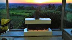 Et værelse med pejs, udsigt til solnedgang og en stol med hynde.