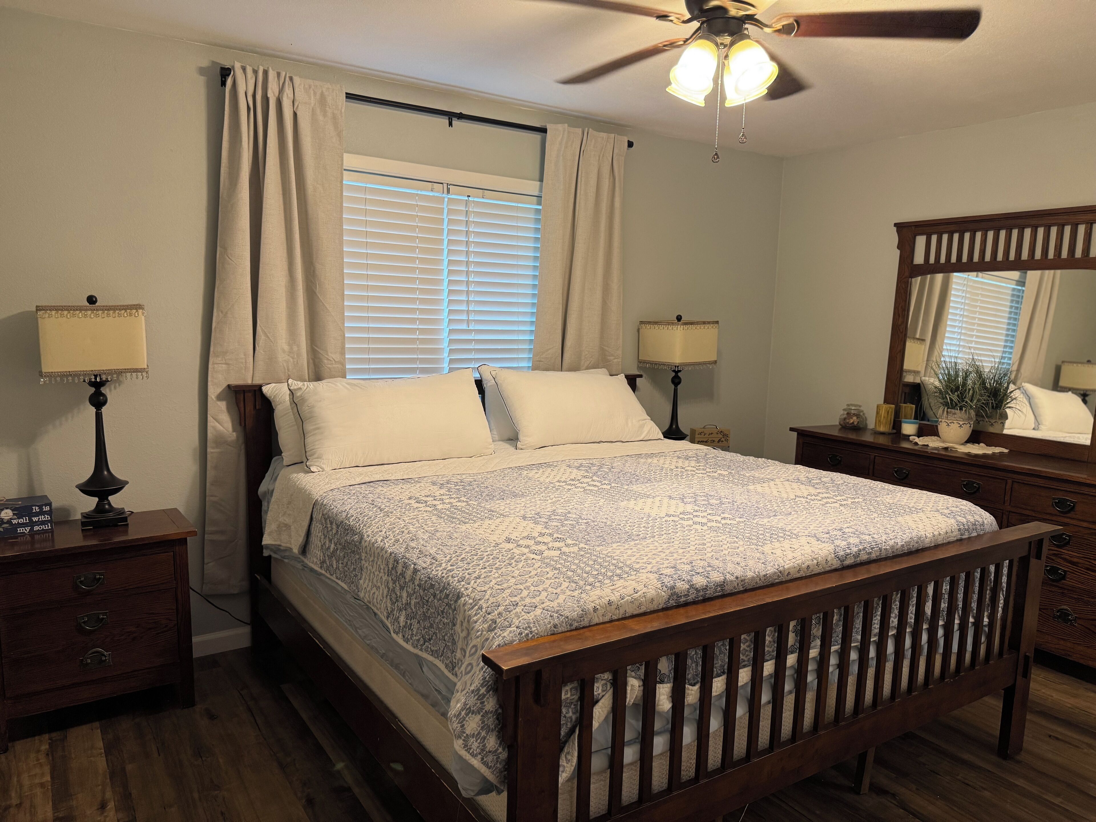 A bedroom with a wooden bed, two bedside tables with lamps, a ceiling fan, and a large mirror.