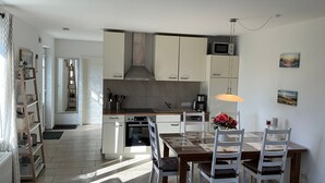 Una cuina moderna amb armaris blancs, un microones i una zona de menjador amb taula i cadires.
