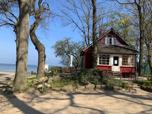 A small, red wooden house with a white window and door, surrounded by trees and a sandy area. - in Hoben mit Grill und Terrasse by Interhome (Alt Jassewitz)