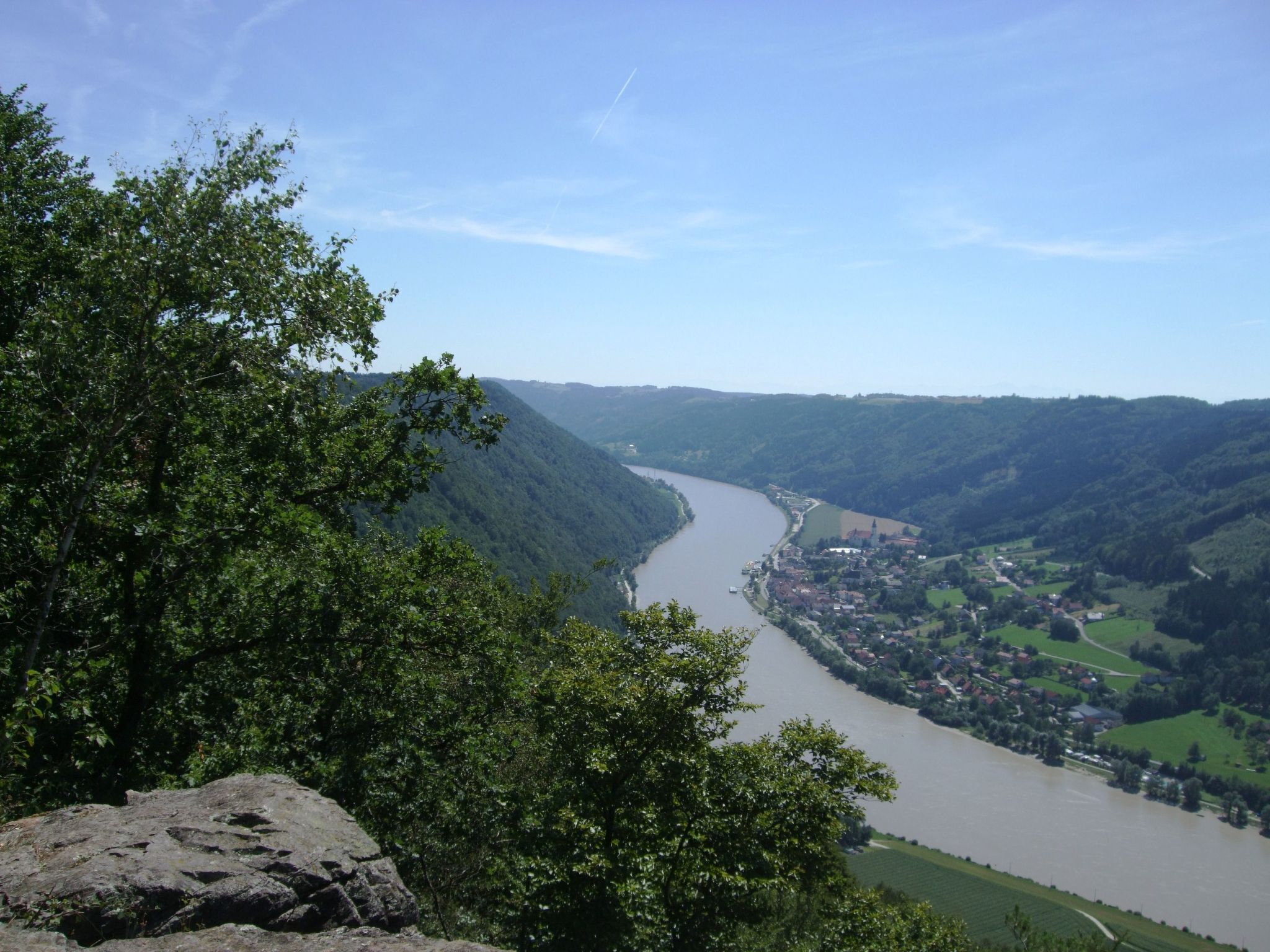 Une rivière serpente à travers une vallée, avec une ville d’un côté et des collines boisées de l’autre.