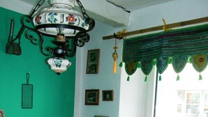 Une pièce chaleureuse avec un banc en bois, une table recouverte d’une nappe colorée, une lampe suspendue et une fenêtre ornée d’un rideau vert.