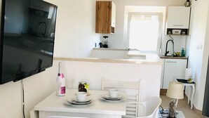A compact living space with a dining area, kitchenette, and a TV mounted on the wall. - Apartment Smokvica by Interhome (Umag/Savudrija)