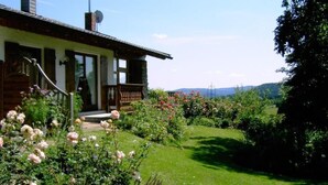 Ett hus med en veranda framför, en trappa och en trädgård med blommor.