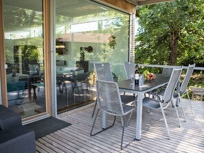 Un espacio de comedor al aire libre con una mesa y sillas de vidrio, una terraza de madera y vistas a la vegetación circundante.