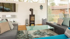 Un salon moderne avec une table basse en verre, deux canapés, une cheminée et une grande fenêtre offrant une vue sur l’extérieur.