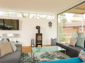 Ein modernes Wohnzimmer mit einem Glastisch, zwei Sofas, einem Kamin und einem großen Fenster mit Blick ins Freie.