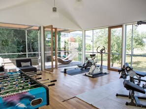 Una habitación amplia con mesa de fútbol de mesa, equipo de ejercicio y grandes ventanales que ofrecen vistas al exterior.