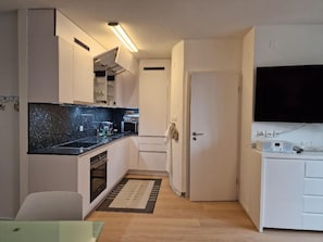A compact kitchen with a black countertop, white cabinets, and a built-in oven. - Cristal 68 Attika by Interhome (Leukerbad)