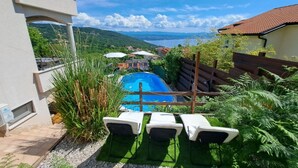 Una piscina con sillones de descanso, rodeada de vegetación y con vistas a un pueblo lejano.