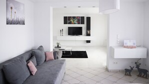 Un salon moderne avec un canapé gris, un téléviseur à écran plat, une console blanche et un plafond doté de panneaux perforés.