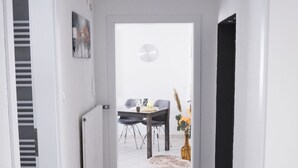 Un couloir avec un tapis à motifs, un coin repas avec une table et des chaises, et un radiateur.