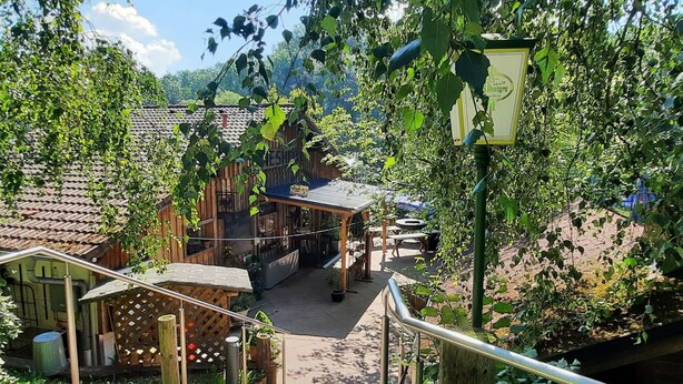 Un bâtiment rustique en bois, doté d’un toit en tuiles, d’un espace extérieur abrité avec des sièges et d’un escalier menant à une terrasse en bois.