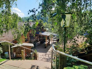 Un bâtiment rustique en bois, doté d’un toit en tuiles, d’un espace extérieur abrité avec des sièges et d’un escalier menant à une terrasse en bois.