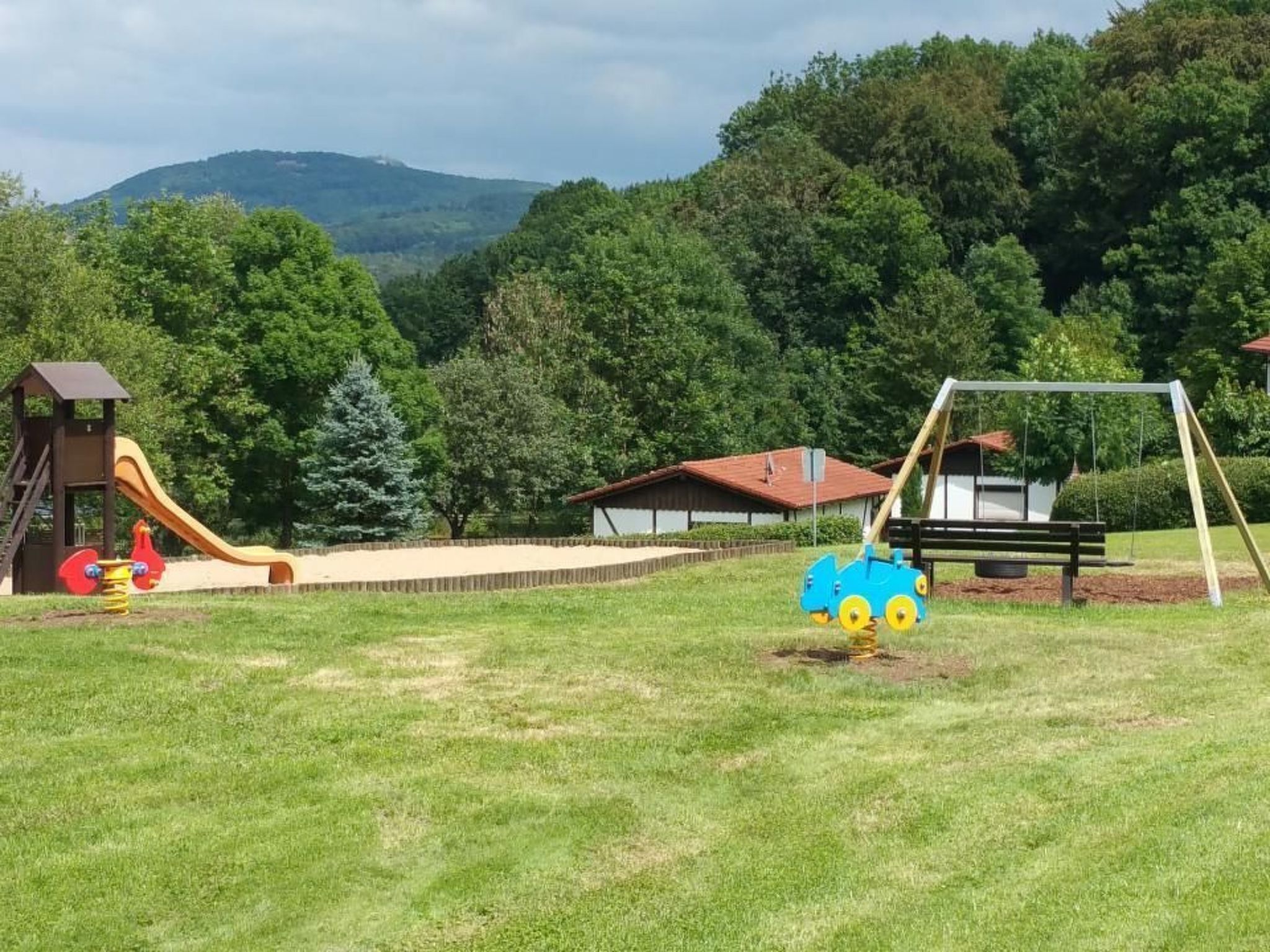 A playground with a slide and swings, surrounded by greenery and houses.