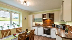 Cocina compacta con zona de comedor, piso de madera y ventana con plantas.