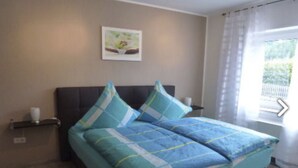 Una camera da letto con un letto, un comodino, un quadro appeso al muro e una finestra con tende.
