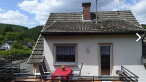 Una piccola casa con tetto in tegole, un camino e un balcone con tavolo e sedie.