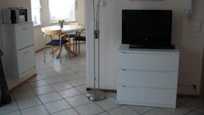 En kompakt opholdsstue med et tekøkken, spiseplads og et fladskærms-tv på et hvidt skab.