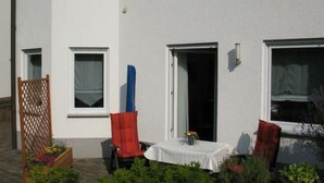 En hvid bygning med en patio, der indeholder et bord, to stole og en blå genstand.