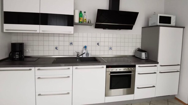 Et moderne køkken med hvide skabe, indbygget ovn, mikroovn og kaffemaskine.