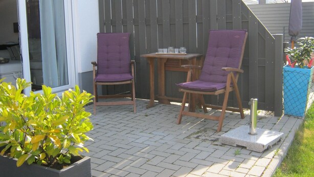 Een terras buiten met twee houten stoelen en een kleine tafel.
