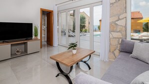 Una sala moderna con un televisor de pantalla plana, una mesa de centro de madera con una planta, un sofá gris y una pared de piedra.