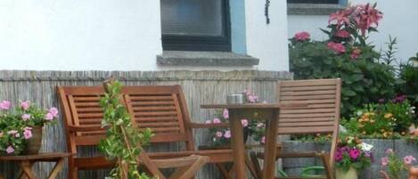 A patio with wooden furniture, a potted plant, and a small garden with flowers.
