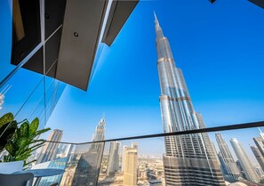 A high-rise building with a distinctive spire, surrounded by other skyscrapers, viewed from a balcony with a clear blue sky. - NEW 2BR Burj Khalifa & Fountain View Suite at Address Opera (Dubai)