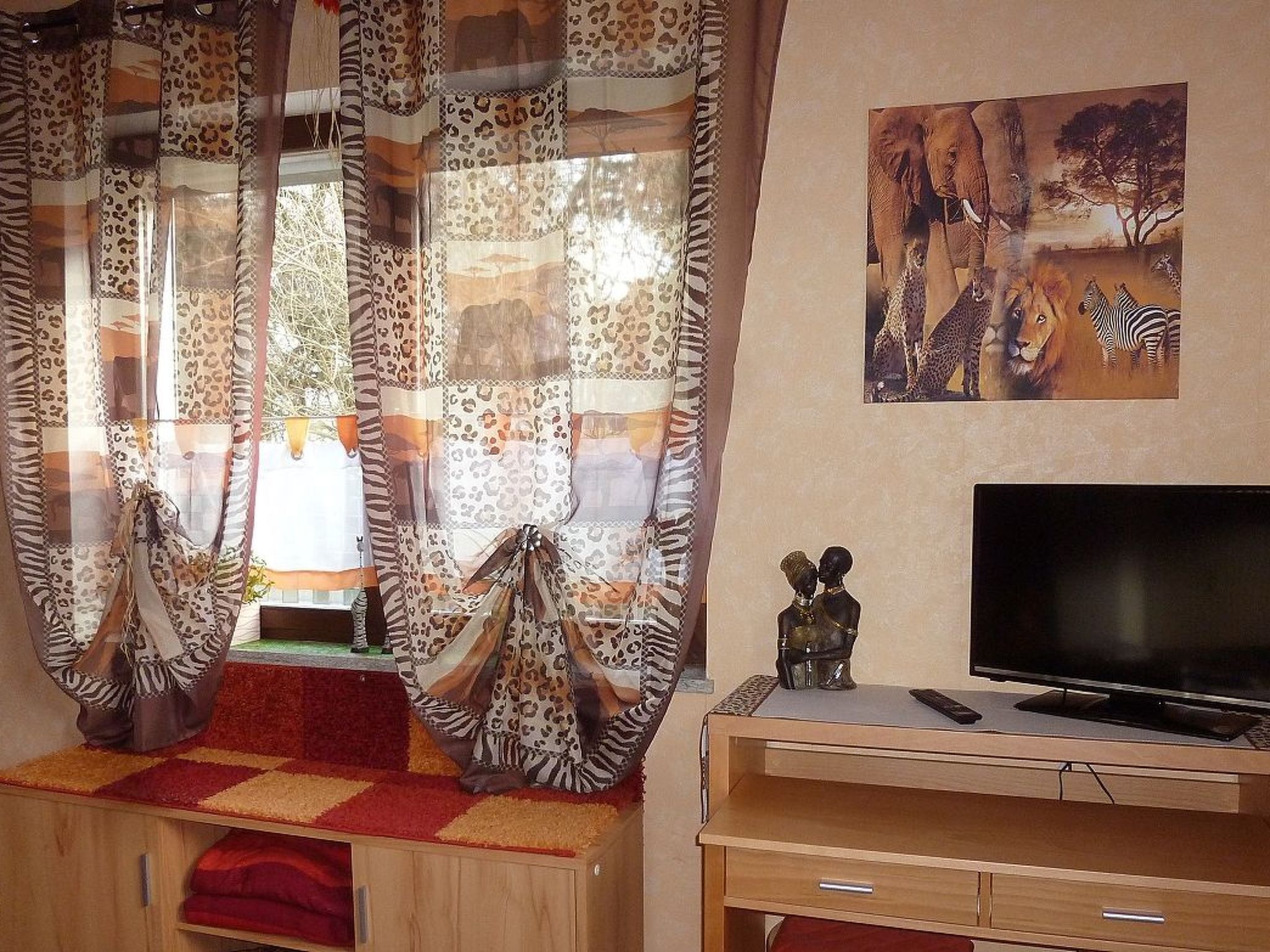 A room with a TV on a wooden stand, leopard-pattern curtains, and a painting of wildlife on the wall.