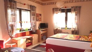 Una habitación con cama, escritorio, televisor y ventana con cortinas.