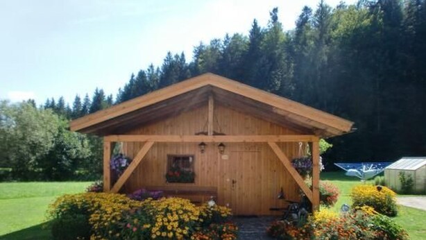 En stuga byggd av trä med ett sadeltak, omgiven av en trädgård med olika sorters blommor och buskar.