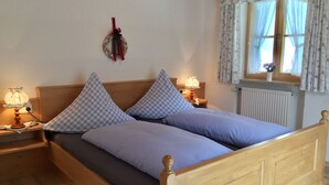 Ein hölzernes Bett mit Kopfteil, zwei Nachttische mit Lampen, ein Fenster mit floralem Vorhang und eine Wanddekoration.