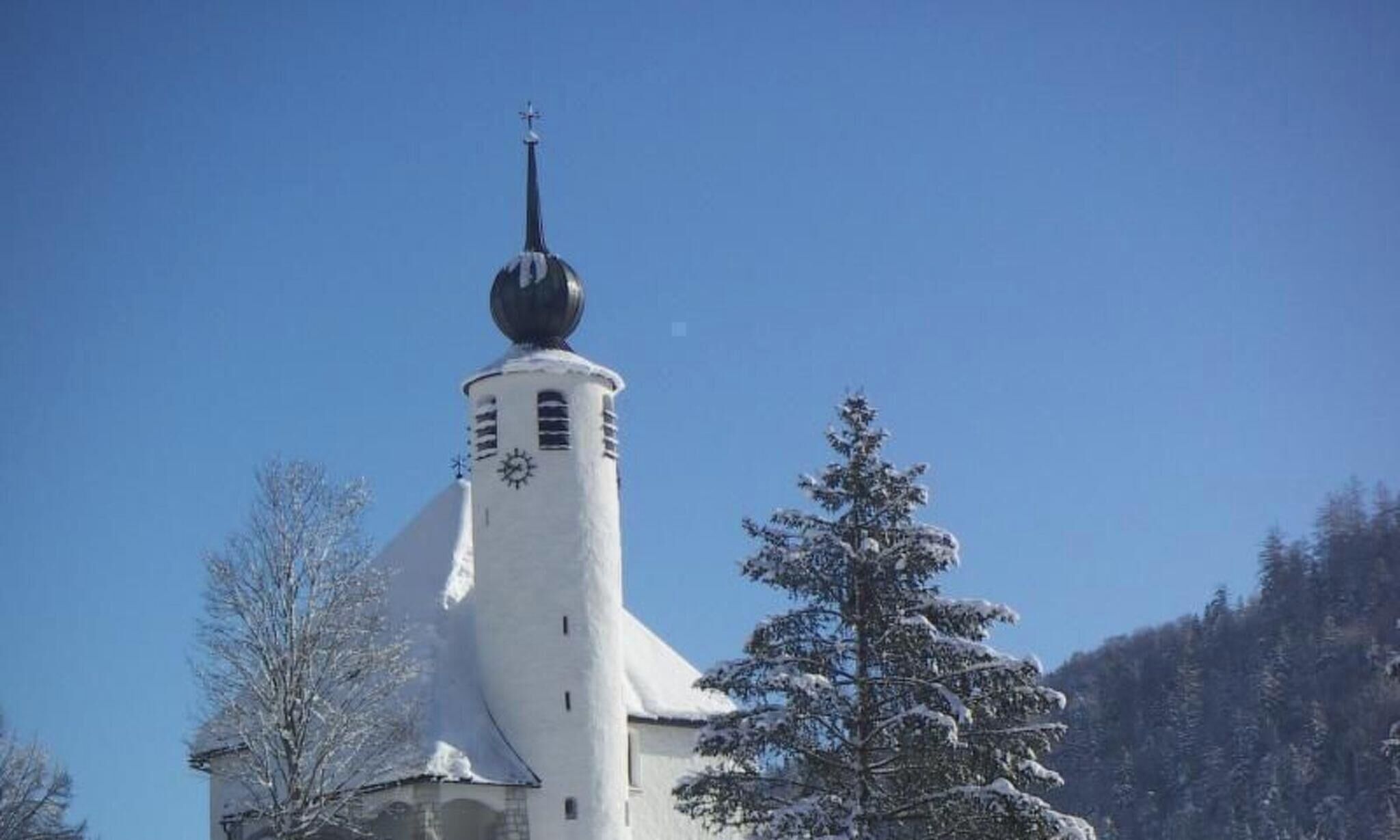 Een kerk met een hoge klokkentoren en een koepel, omringd door met sneeuw bedekte bomen.