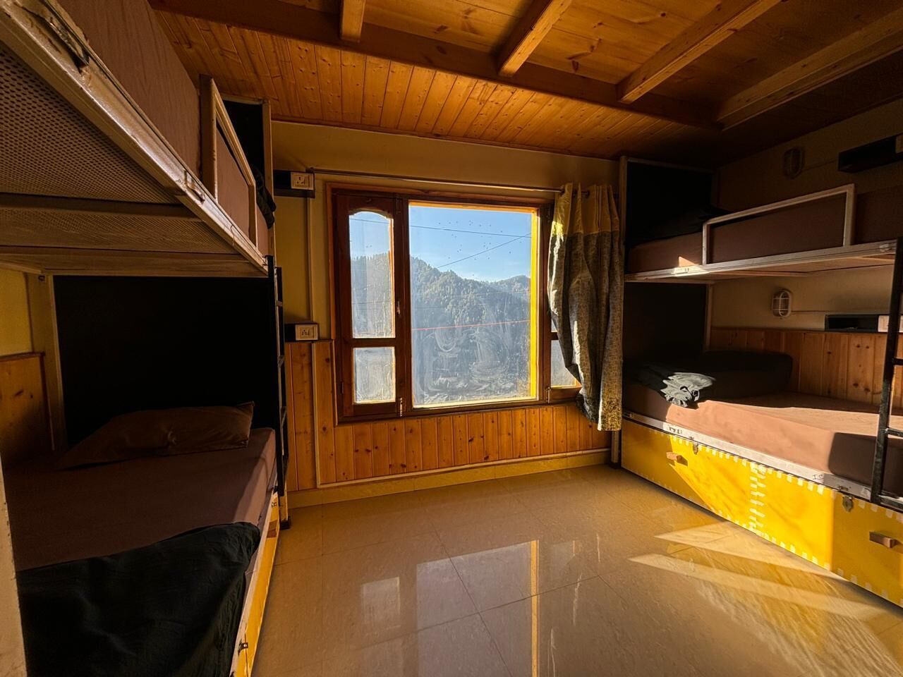 Habitación compacta con literas, un ventanal con vistas a la montaña y paredes de madera.