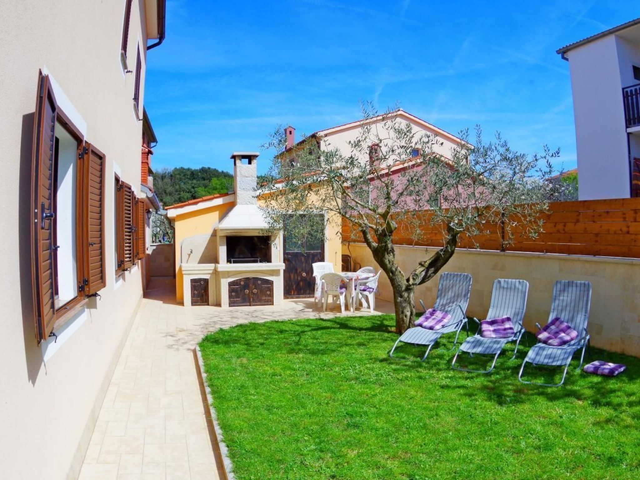 A backyard with a barbecue area, a small tree, and several lounge chairs.