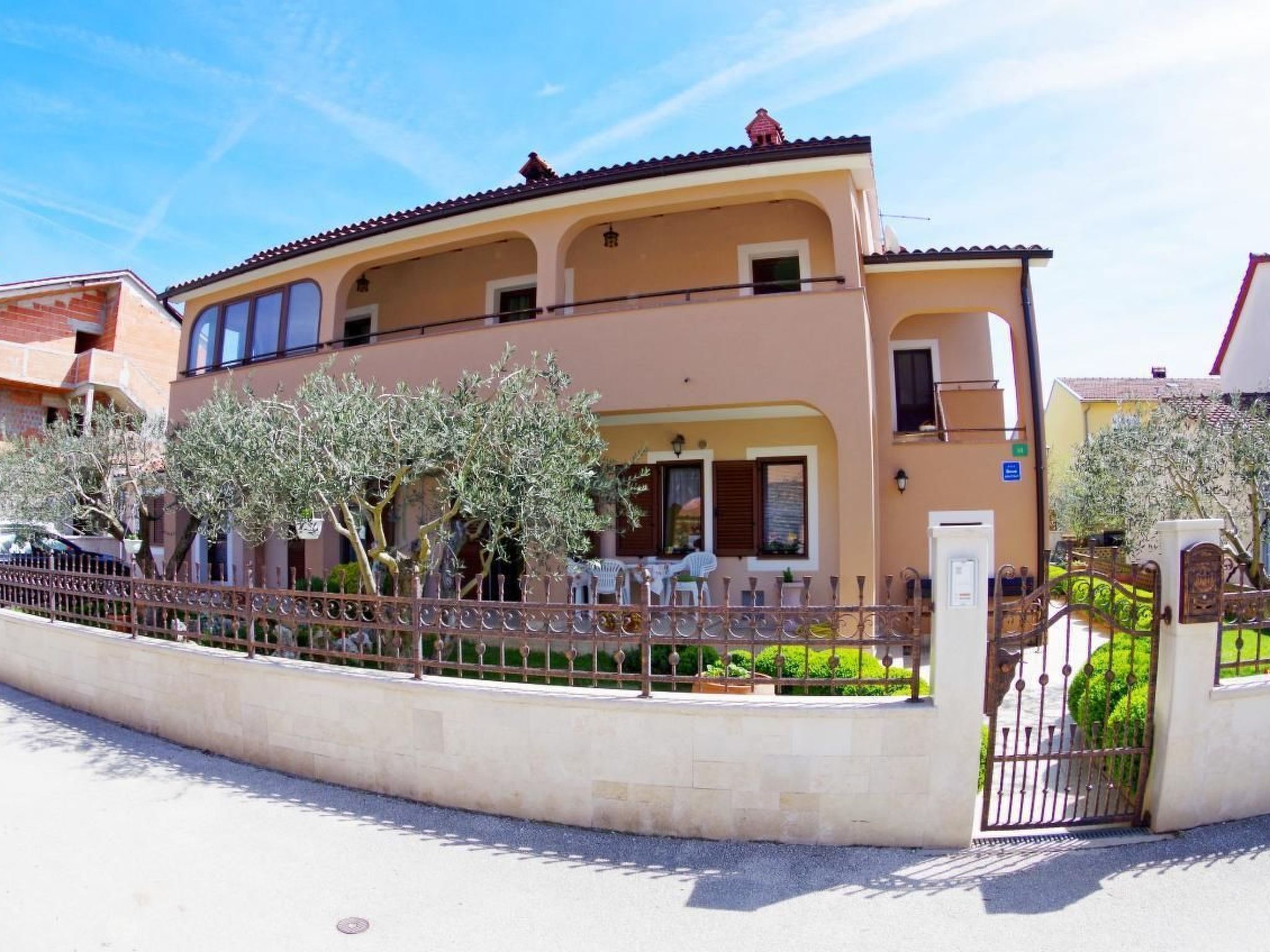 A two-story building with a beige facade, a balcony on the upper floor, and a gated entrance.