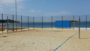 En sandvolleyspillplan med nät, omgiven av ett staket, och en blå byggnad i bakgrunden.