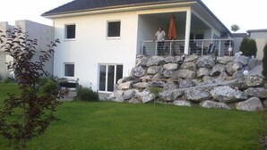 A two-story house with a stone retaining wall, a covered patio, and a lawn. - Wohnung mit großer Gartenterrasse und Ausblick by Interhome (Argenbühl)
