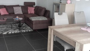 A modern living room with a brown sofa, a glass coffee table, a wooden dining table, and a white chair. - Wohnung mit großer Gartenterrasse und Ausblick by Interhome (Argenbühl)
