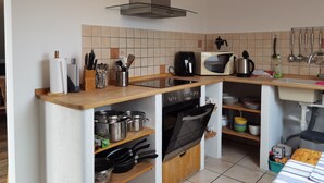 Eine kompakte Küche mit Einbauofen, Mikrowelle und Kaffeemaschine. Es gibt Regale mit Töpfen und Pfannen sowie verschiedene Küchenutensilien.