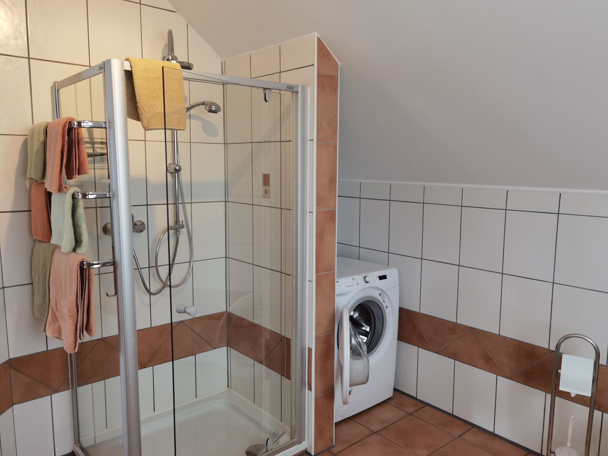 Kylpyhuoneessa on lasiseinällä varustettu suihku, pesukone ja pyyhkeet ripustettuina pyyhetelineeseen.