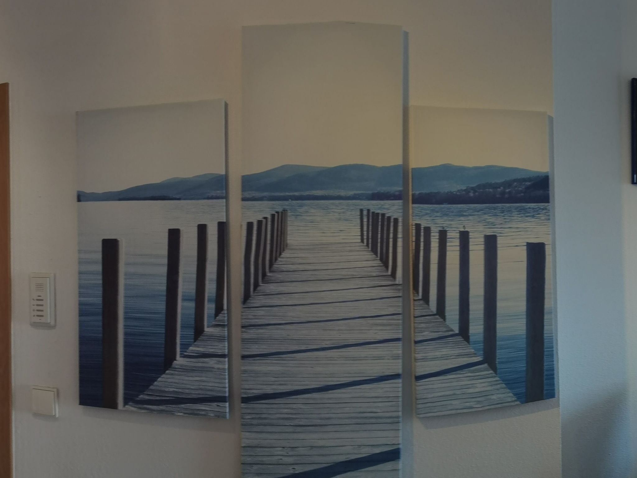 A painting of a wooden pier extending into a body of water with mountains in the background.