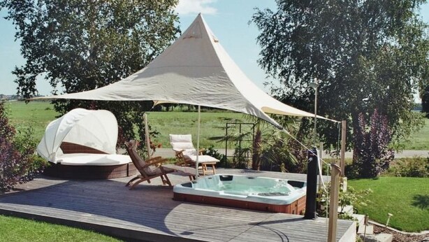 Eine Terrasse mit Whirlpool, Liegestühlen und Sonnensegel.