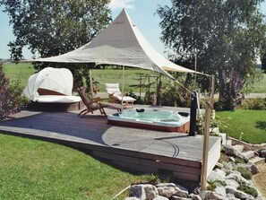 Eine Terrasse mit Whirlpool, Liegestühlen und Sonnensegel.