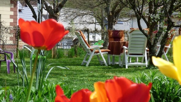 En have med røde og gule tulipaner, hvide liggestole og en grøn stol med brun hynde.